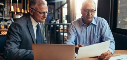 two men discussing over a document with a laptop on the table